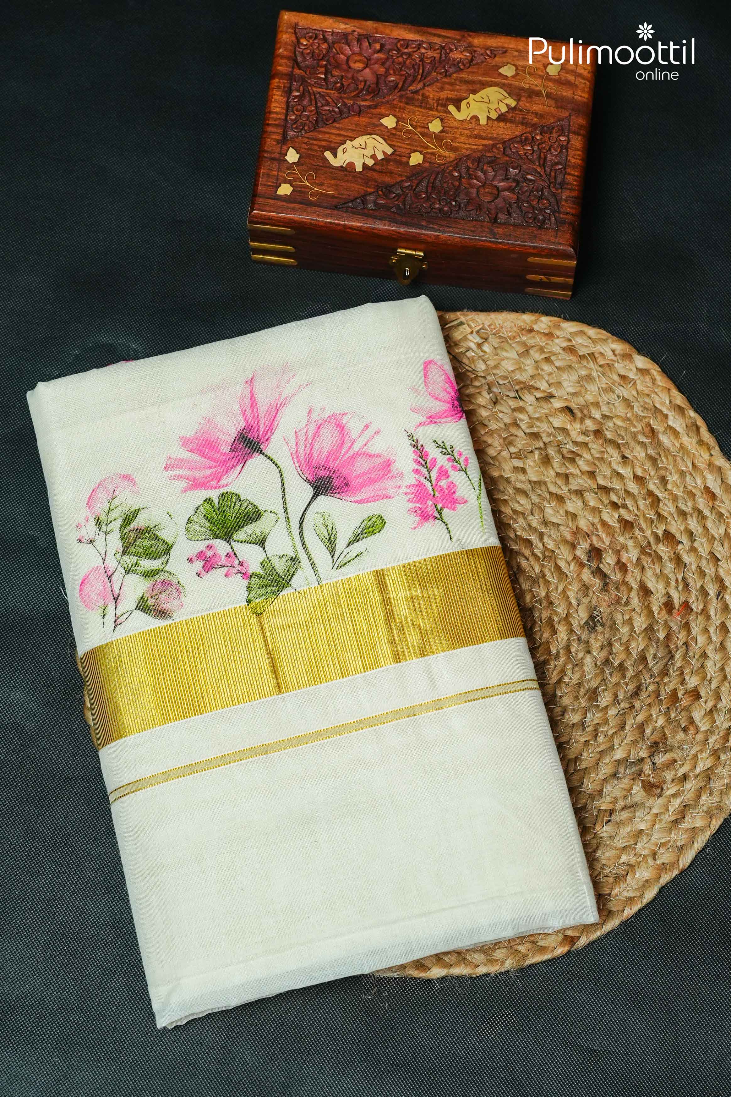 Folded off white Kerala set saree with pink floral print and broad golden tissue border, displayed on surface.
