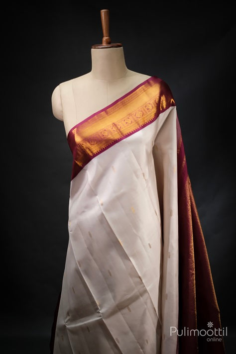 Off White Pure Kanchipuram Silk Saree with Golden Zari Buttas and a Contrast Maroon Border.