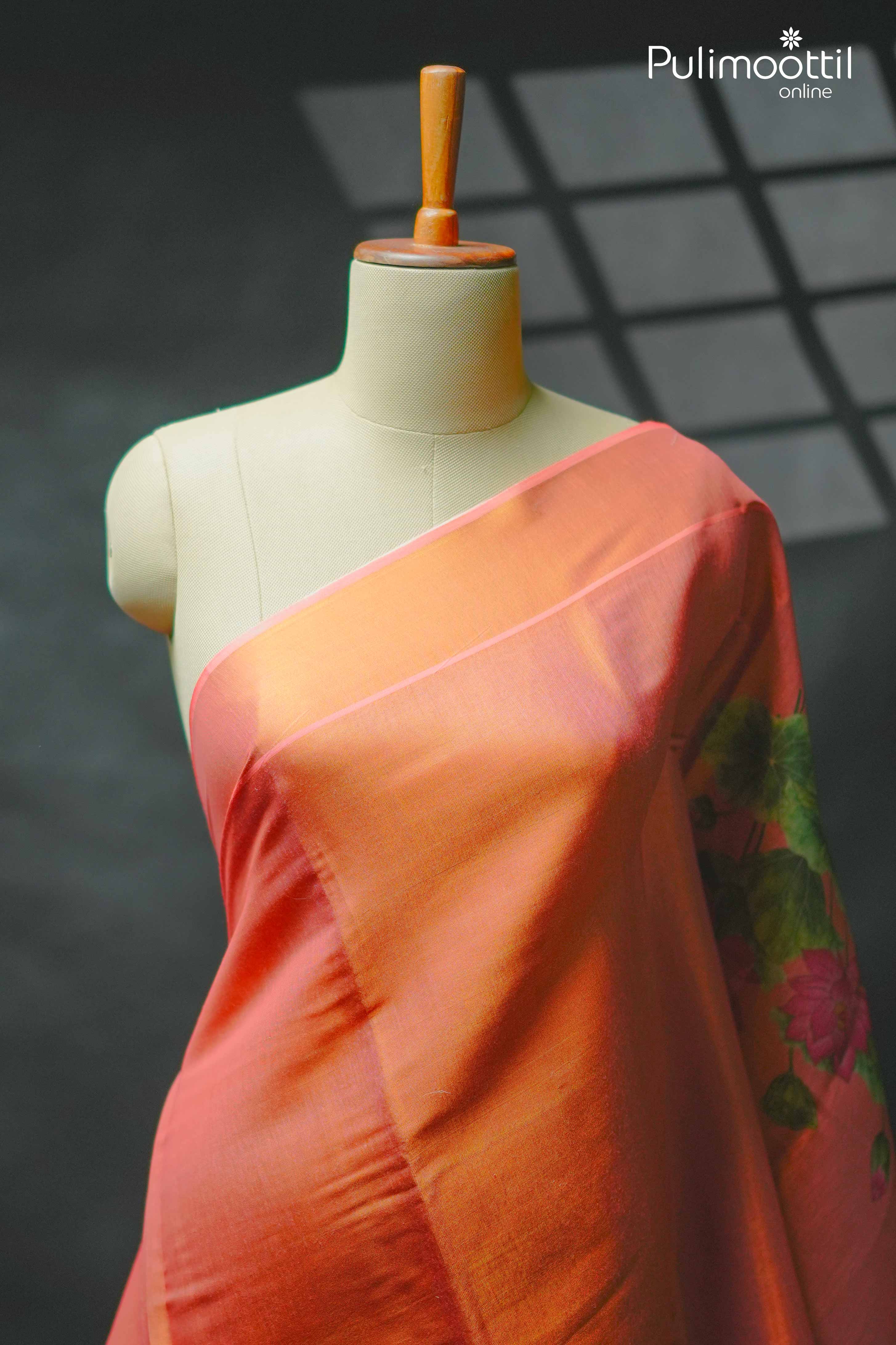 Orange Kerala tissue saree draped on mannequin, featuring plain body and floral lotus print near pallu border.