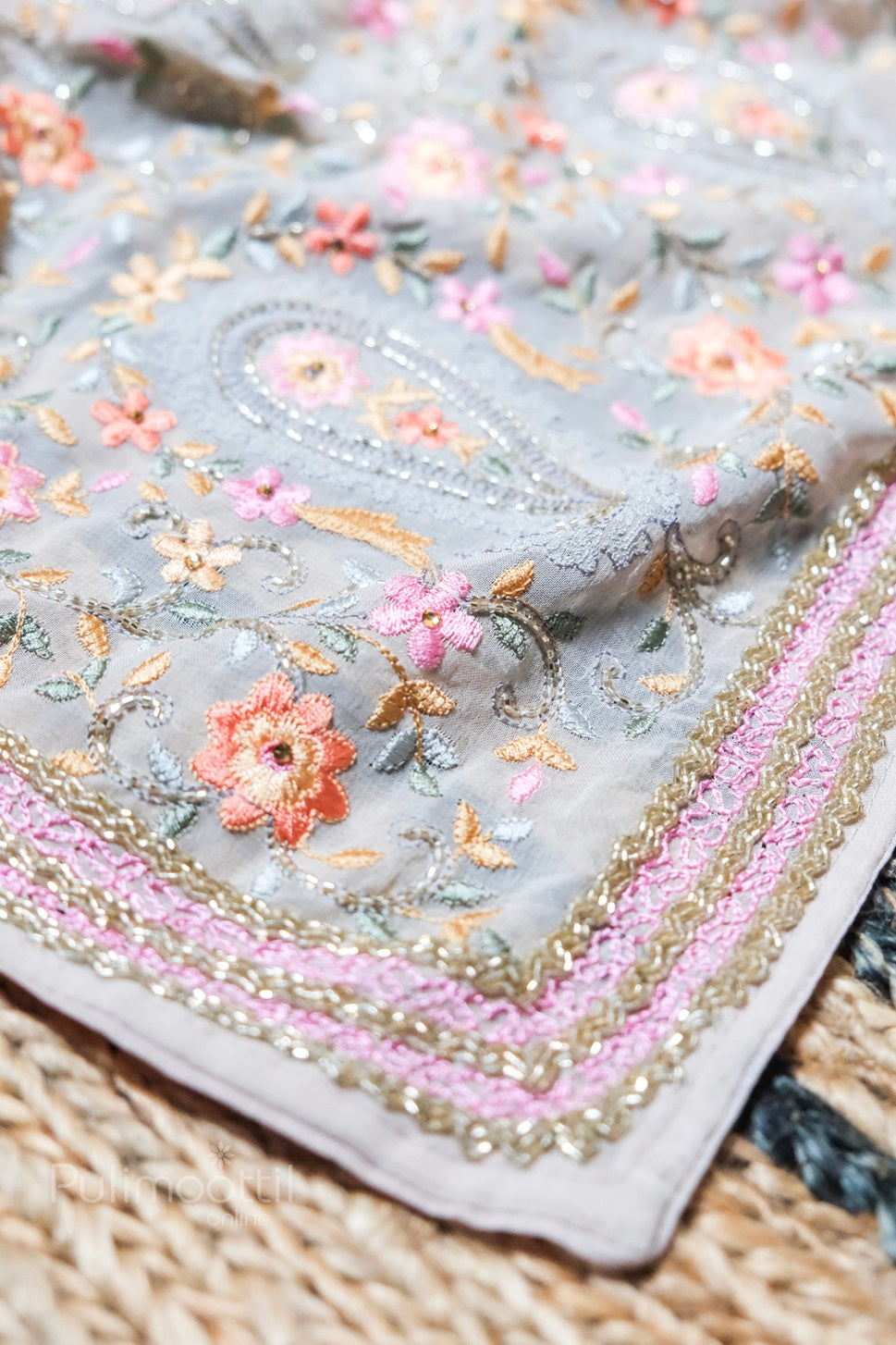 Close-up of light grey net saree pallu with intricate pink and gold embroidered border and pastel floral paisley design
