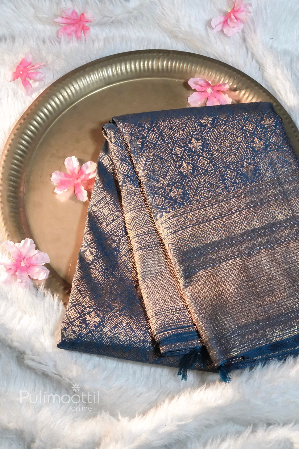 Rich navy blue Banarasi silk saree with intricate golden zari weaving, folded neatly on a brass plate with floral decor—ideal for bridal or festive wear.