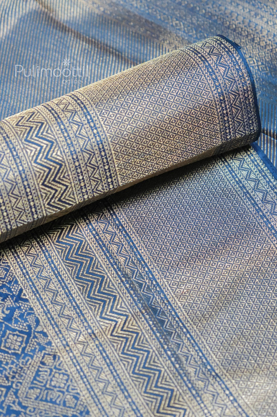 Close-up of navy blue Banarasi silk saree with intricate golden zari weaving and zigzag geometric patterns, showcasing rich texture and traditional detailing.