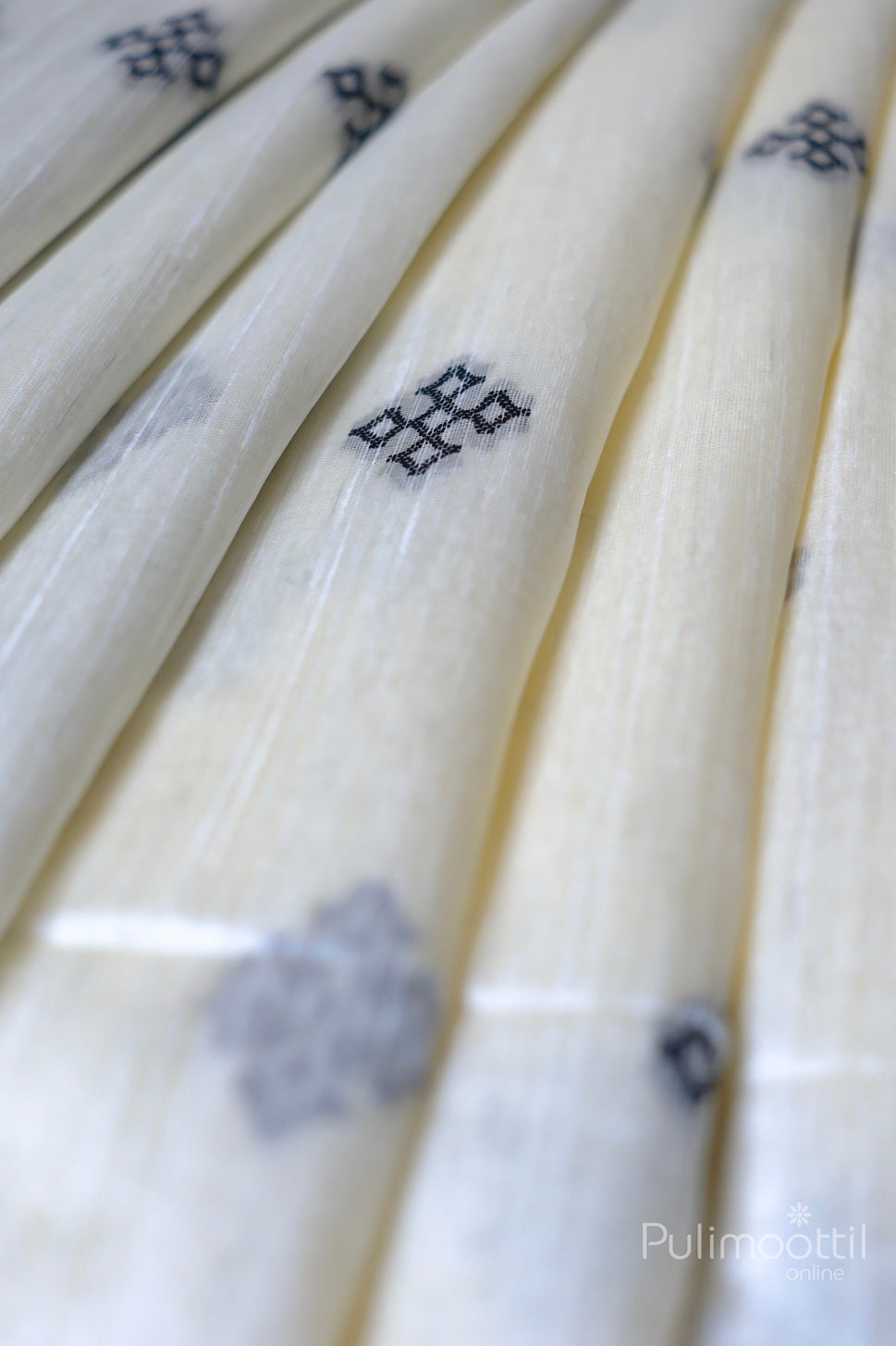 Detailed close-up of off-white semi jute silk saree with black Kutch work buttas, showcasing the flowing fabric and intricate border design.
