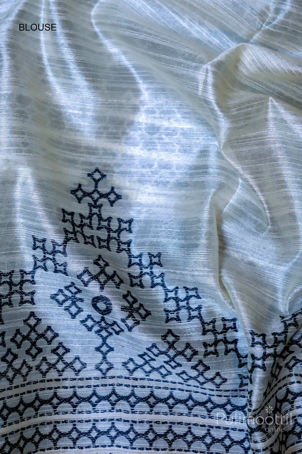 Blouse piece of Close-up of off-white saree with black Kutch work buttas and Kutch work border, showing soft, flowing fabric with geometric patterns.