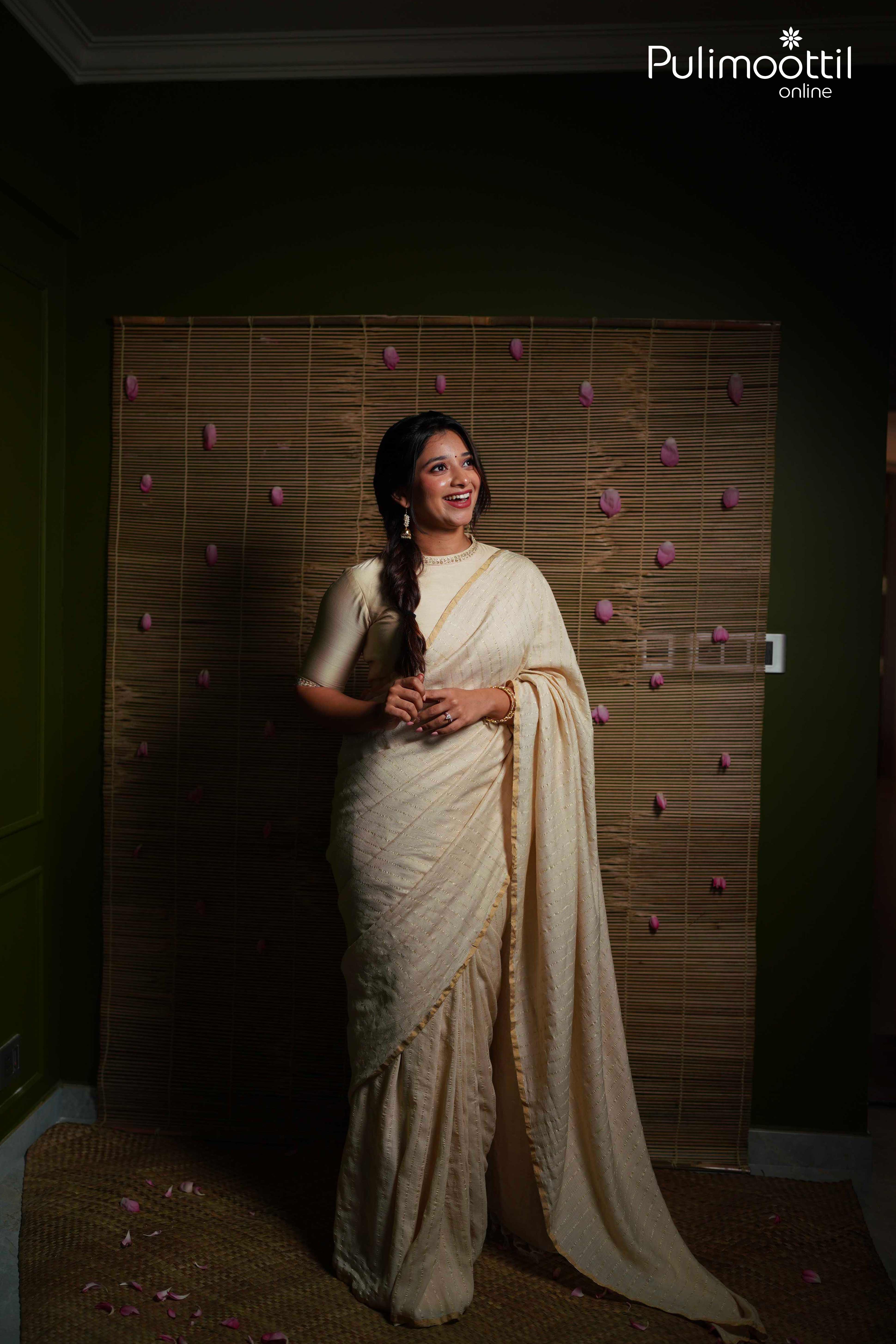 Woman draped in cream pure silk tissue saree with silver zari stripes and elegant thin gold border, perfect for traditional occasions.