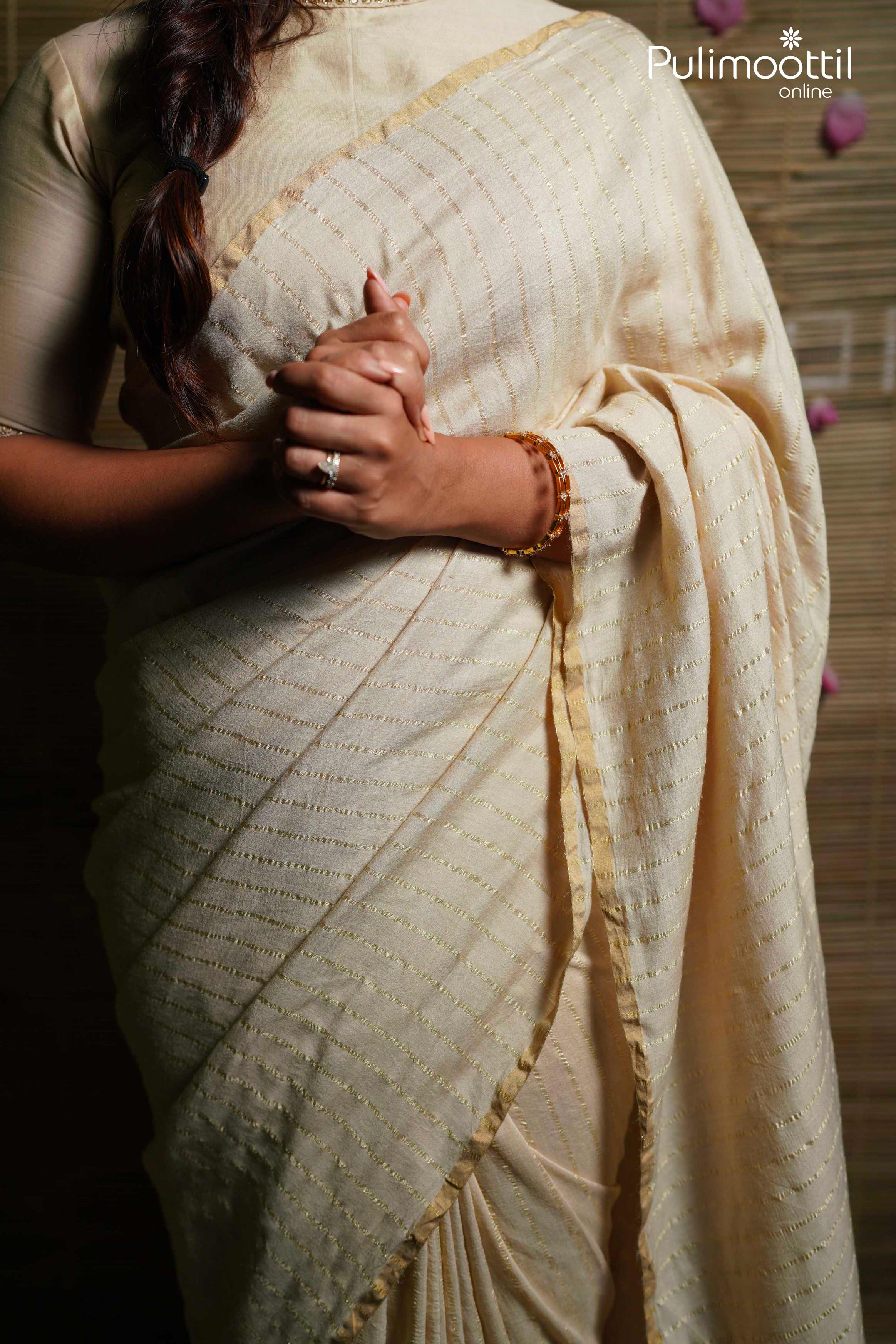 Cream pure silk tissue saree with silver zari stripes and thin gold border, detailed close-up of fabric drape and texture.