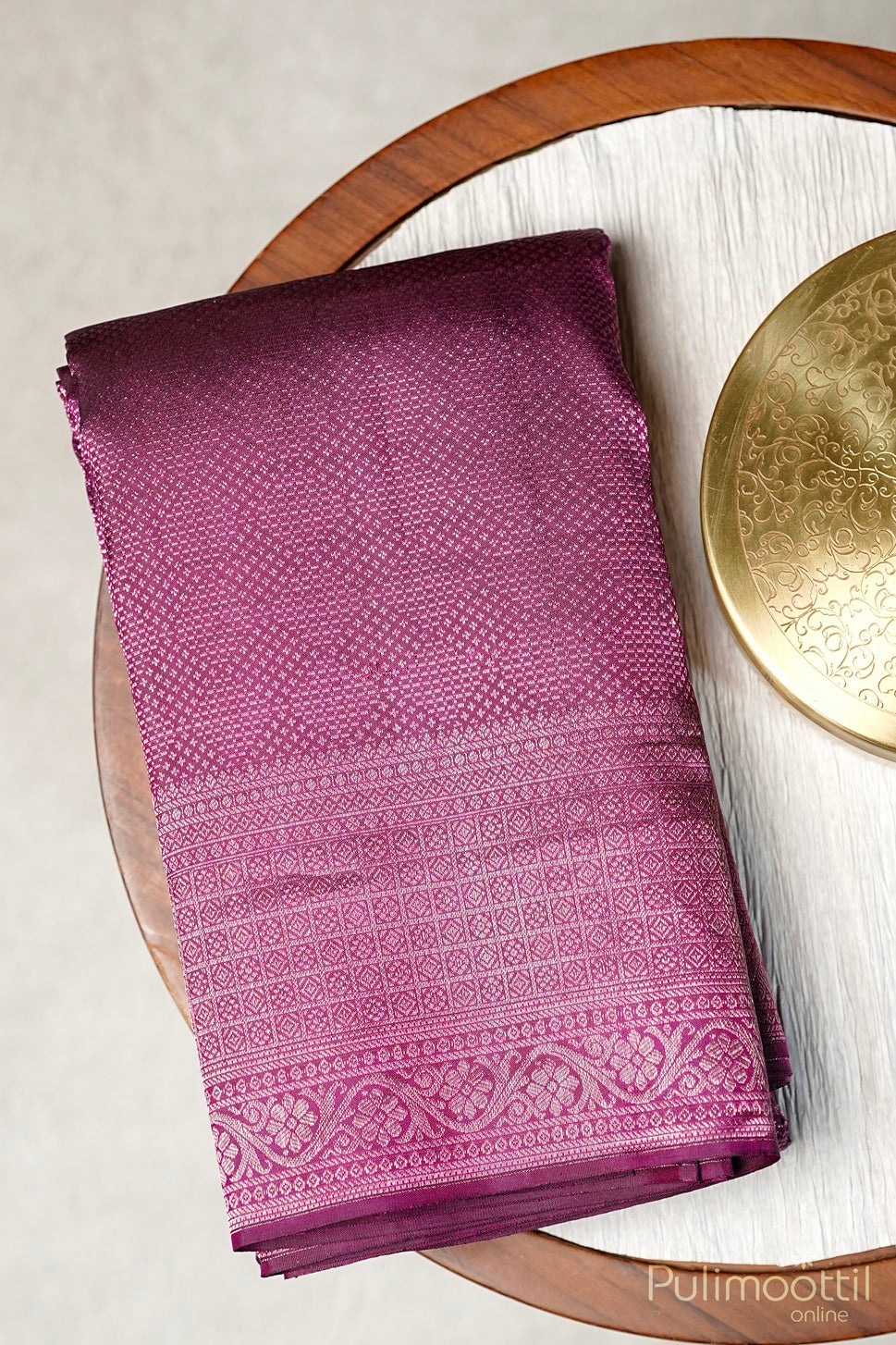 Folded deep purple Kanchipuram brocade saree with antique gold zari border displayed on a wooden surface.
