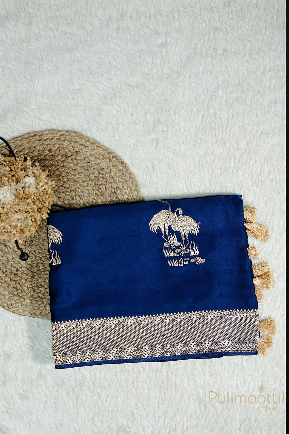 Folded royal blue Uppada silk saree with golden zari bird motif and geometric pattern zari border, featuring decorative tassels at the edge.