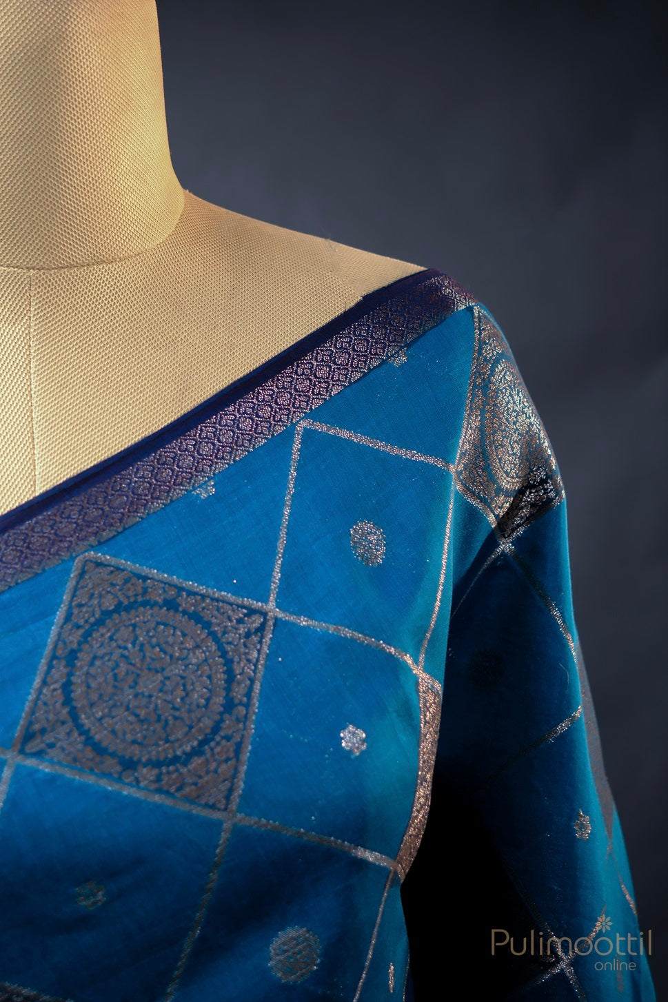 Close-up of the turquoise blue saree with silver zari square design and contrast border, capturing the rich texture and intricate detailing that make it an ideal choice for weddings and cultural events.