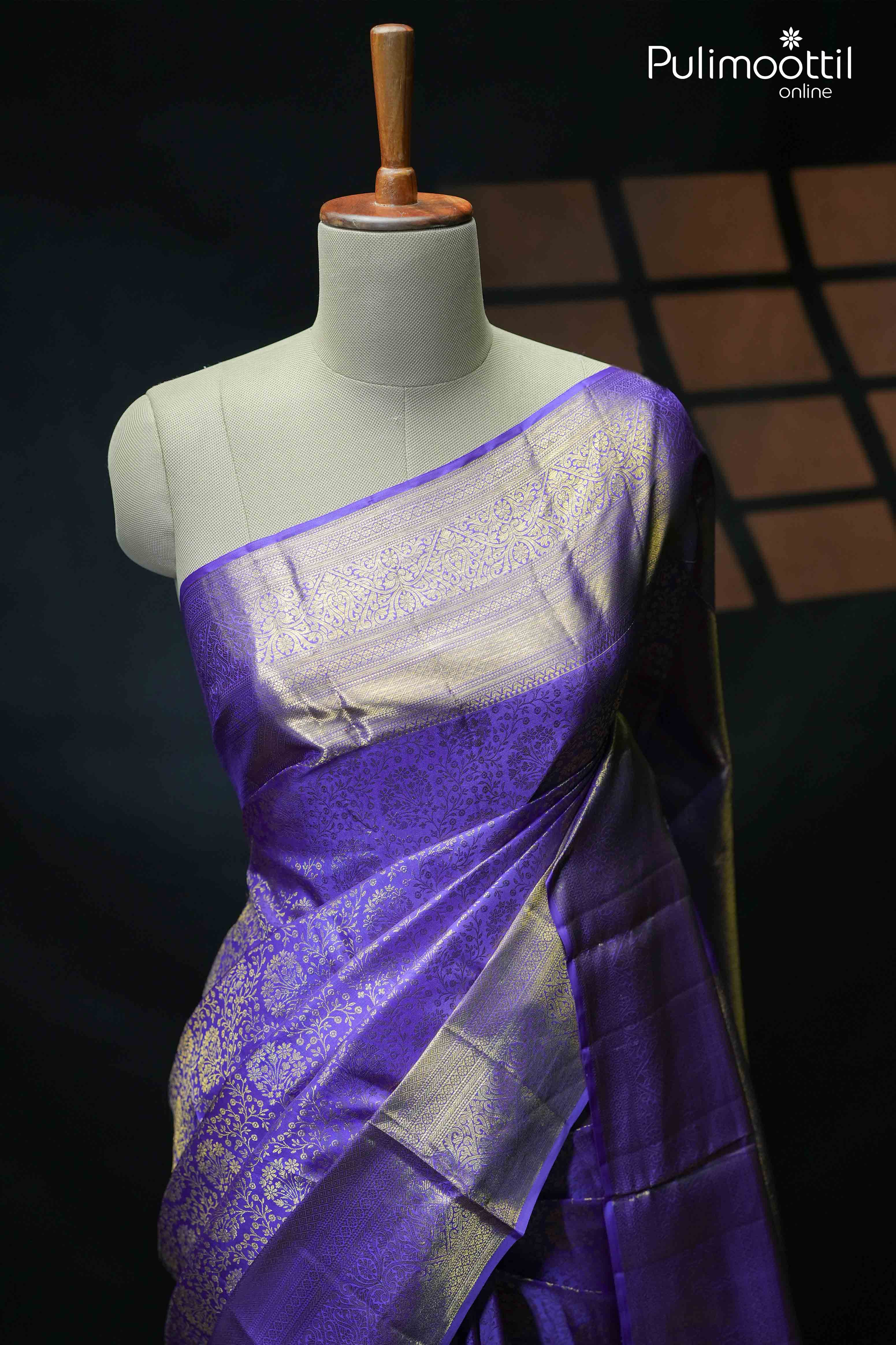 Violet Kanchipuram wedding saree with golden zari floral brocade and geometric patterns, elegantly draped on a mannequin, perfect for weddings and special occasions.