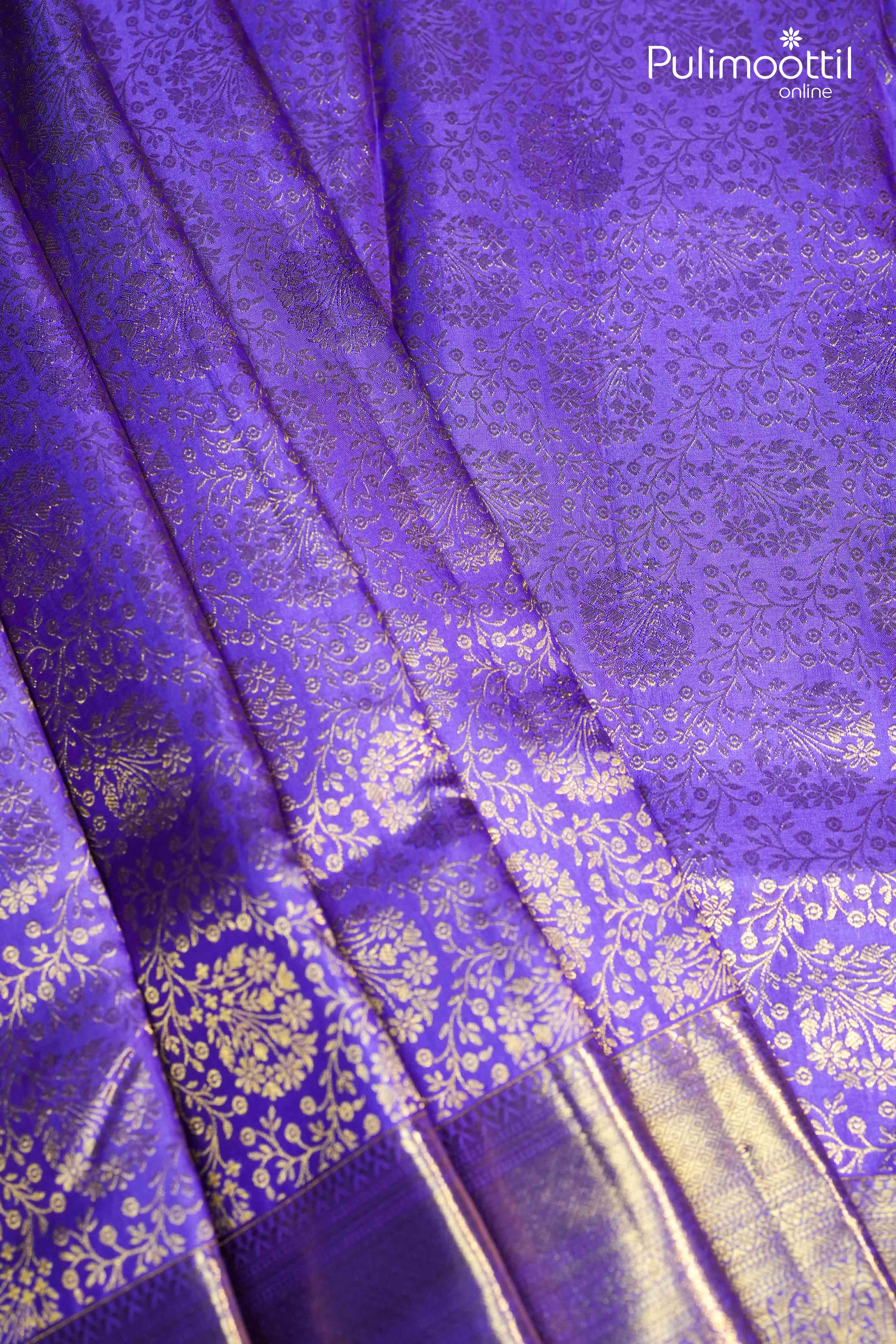 Close-up of a violet Kanchipuram saree with golden zari floral design, showcasing the rich texture, intricate patterns, and glossy finish of the fabric.