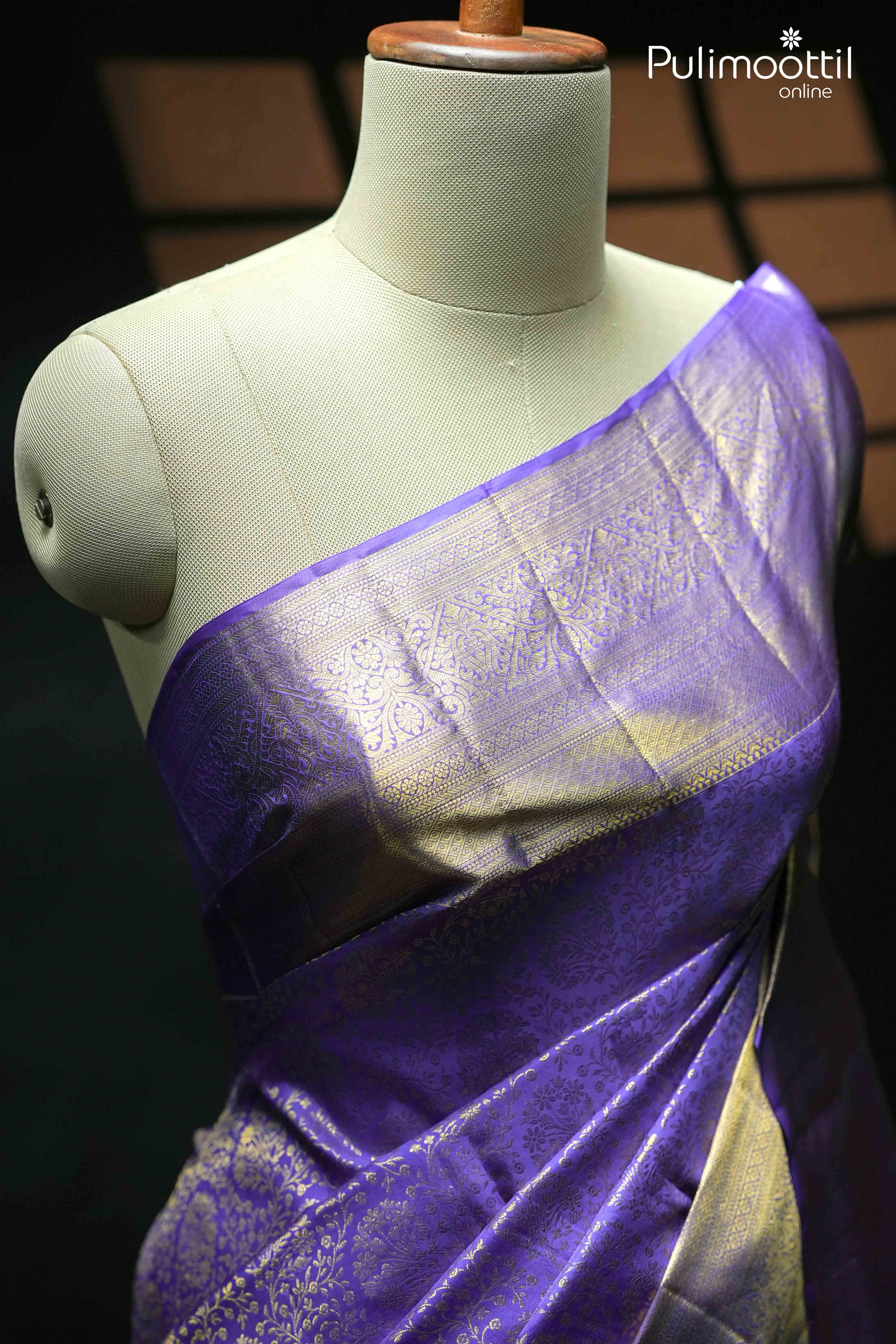 Close-up of a violet Kanchipuram saree with golden zari floral and geometric patterns, elegantly draped on a mannequin, highlighting its luxurious sheen and detailed design.