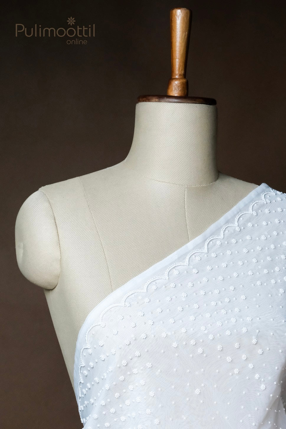 White embroidered net saree with floral dot pattern and scalloped pearl border draped on mannequin bust