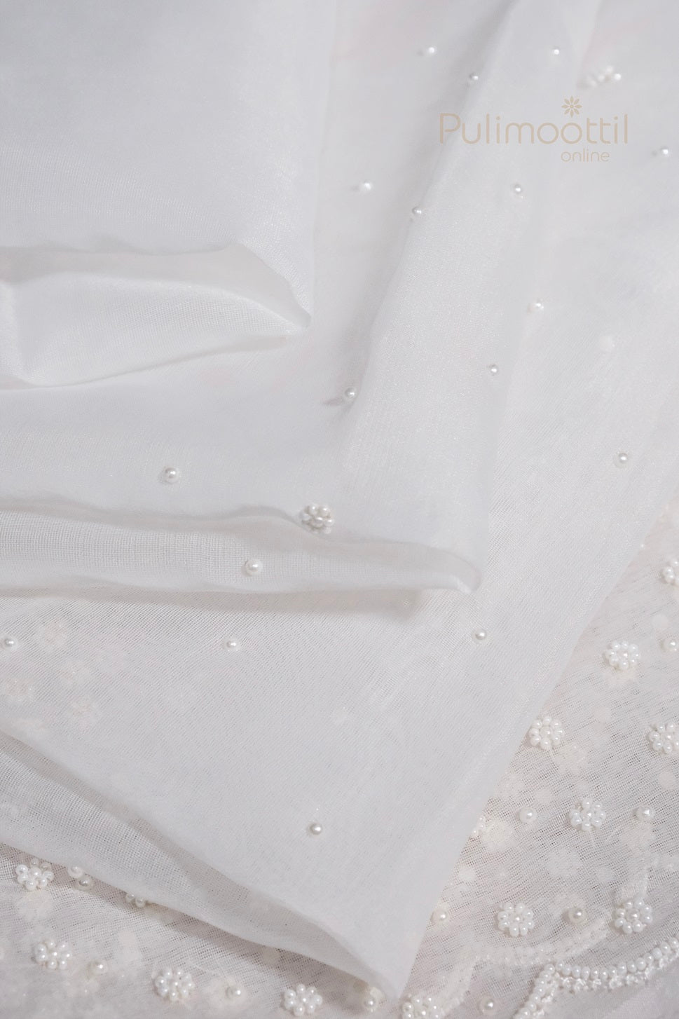 White pearl embroidered net saree with matching plain blouse piece displayed on fabric background