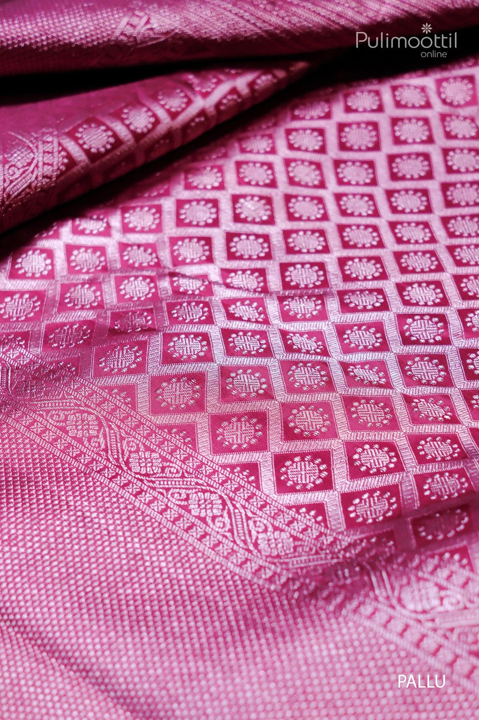 Close-up view of the pallu of a pink silk saree, featuring a detailed geometric pattern with square motifs and floral designs in a rich, glossy texture, with a traditional border along the edges.