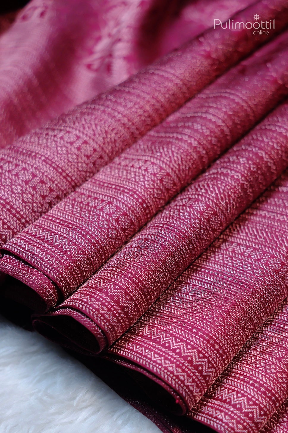 Close-up of folded pink fabric with intricate geometric and floral patterns, showcasing the luxurious texture and sheen of the silk, emphasizing the fine craftsmanship and detailed design of the saree.