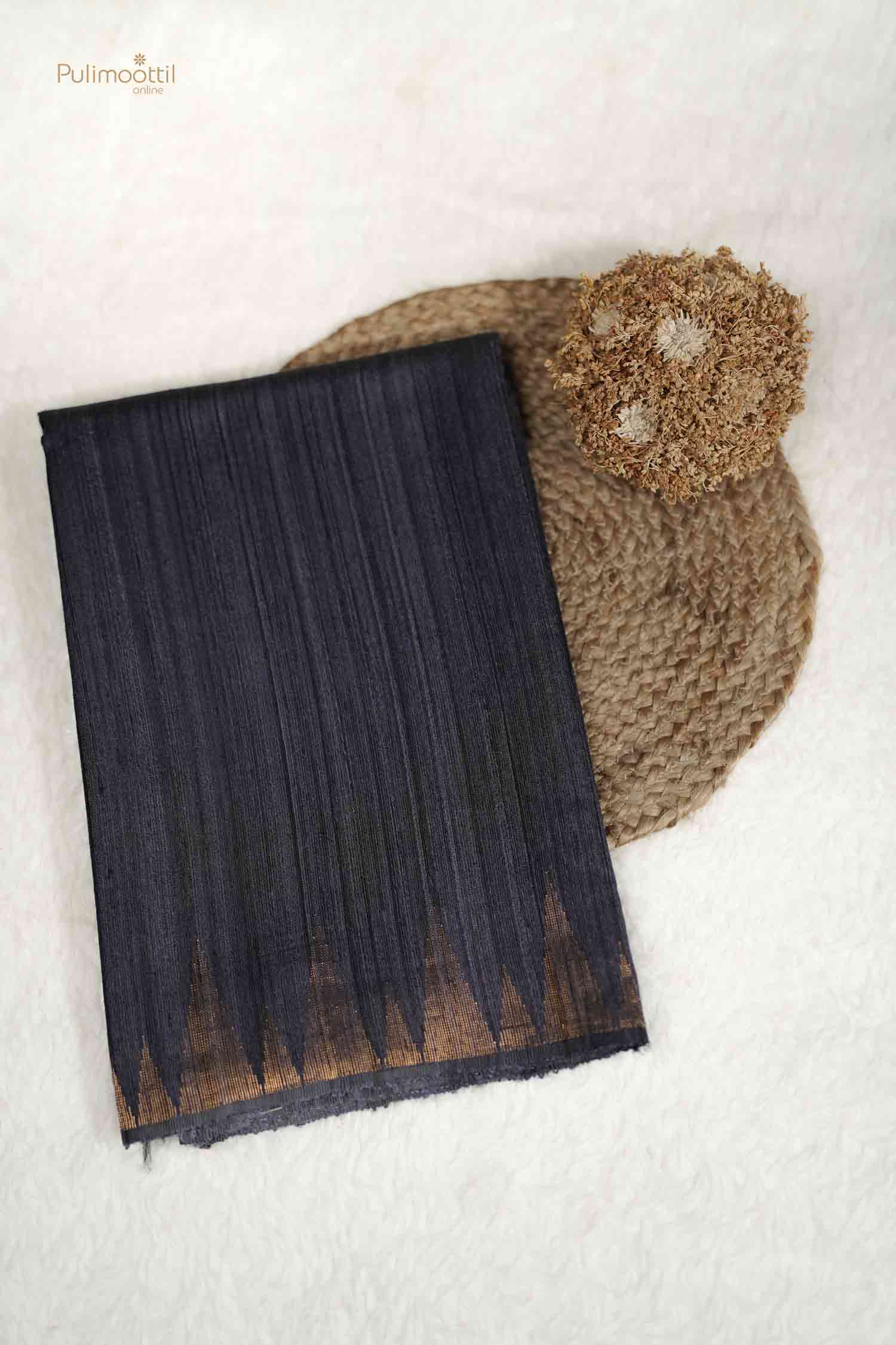 Top-down product shot of a folded Black Raw Silk Saree with a prominent copper/gold serrated (zig-zag) woven border detail.