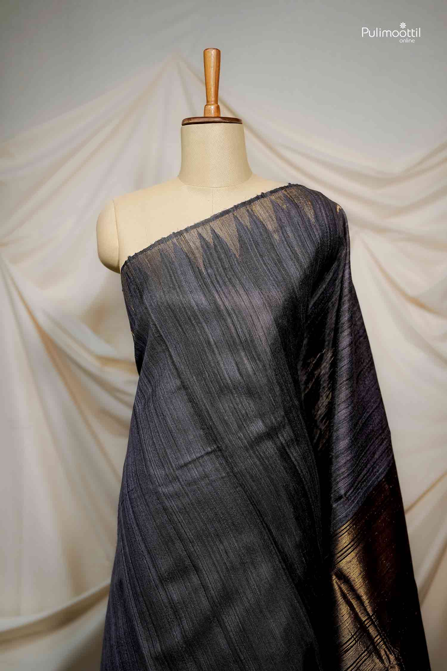 Mannequin drape of the Black Tussar Saree, showing the diagonal slub texture and the beginning of the rich gold woven pallu section.