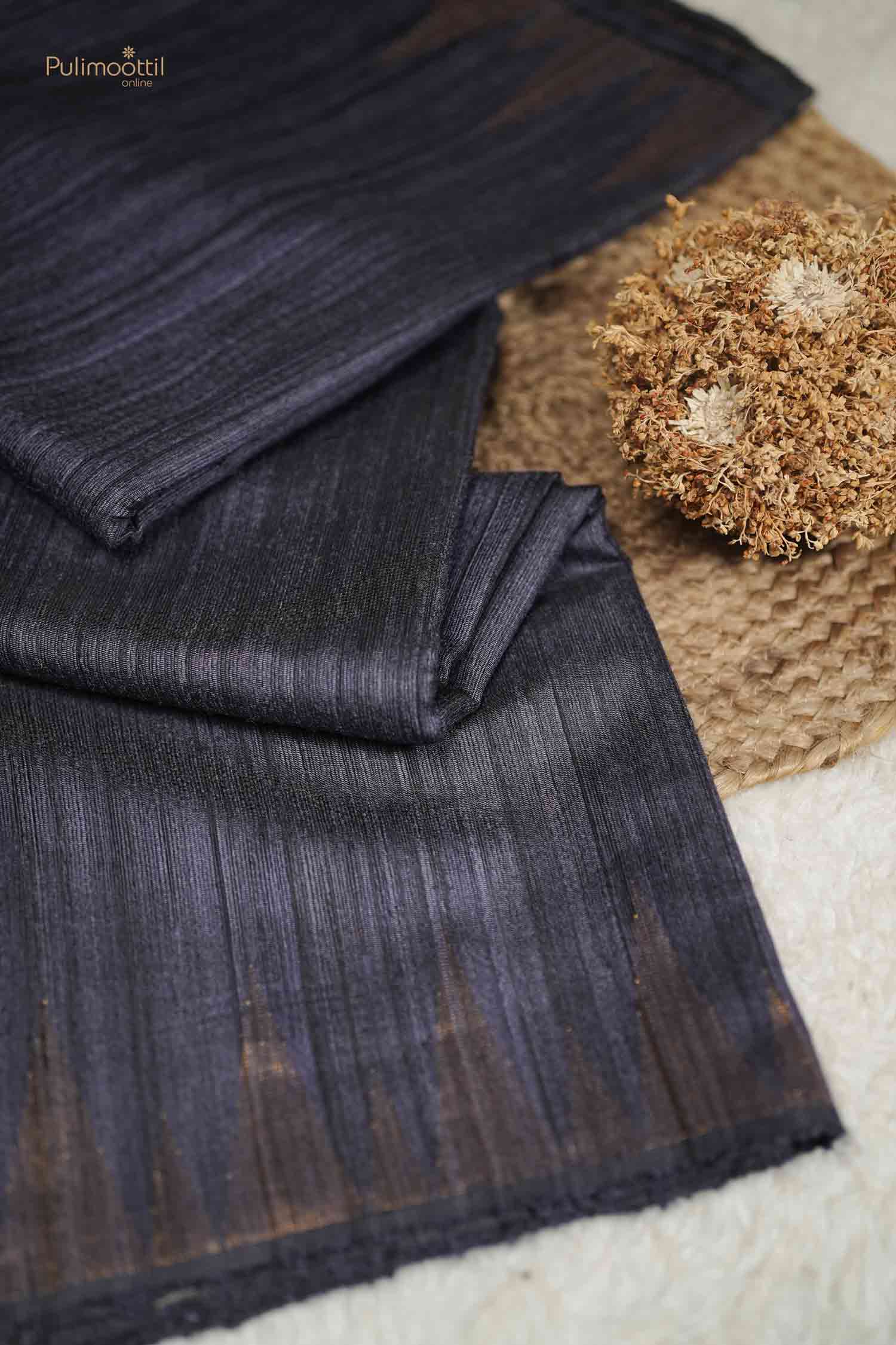 Close-up of the Black Tussar Silk Saree fabric folds, showing the natural slub texture and the shimmer of the gold weave