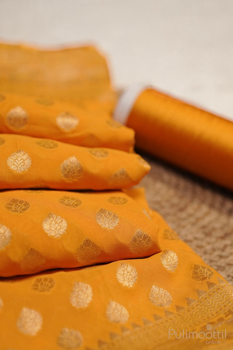 Folded mustard yellow Banarasi saree with golden buttas and border, paired with thread spool.