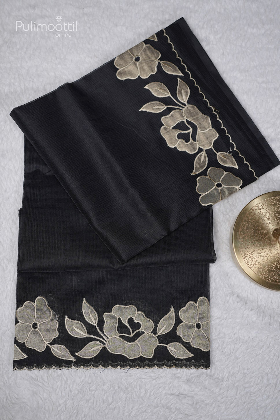 Close-up of black netcotta saree showing detailed beige floral applique and scallop border on fabric.
