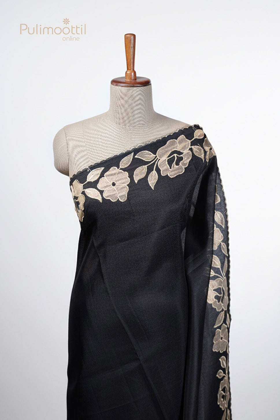 Black netcotta saree draped on mannequin, featuring applique floral border with scallop edges.