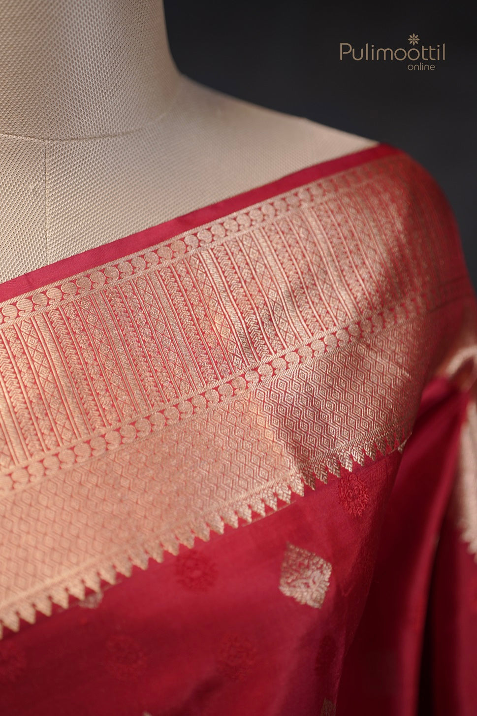 Chilli red Kanchipuram saree draped on a mannequin, showcasing golden buttas and designer border.