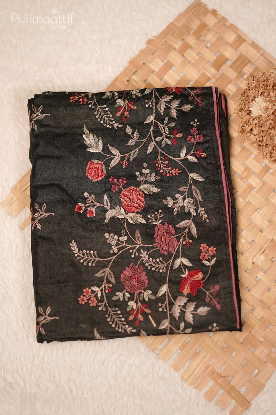 Folded black saree with intricate red and white floral embroidery, featuring a contrasting piping along the edges.