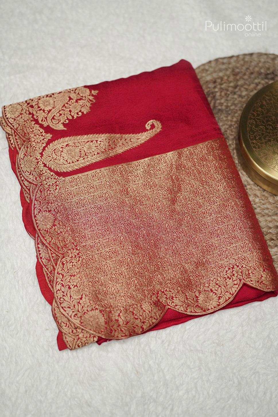 Folded chili red Banarasi silk saree with golden mango motif border and intricate pallu