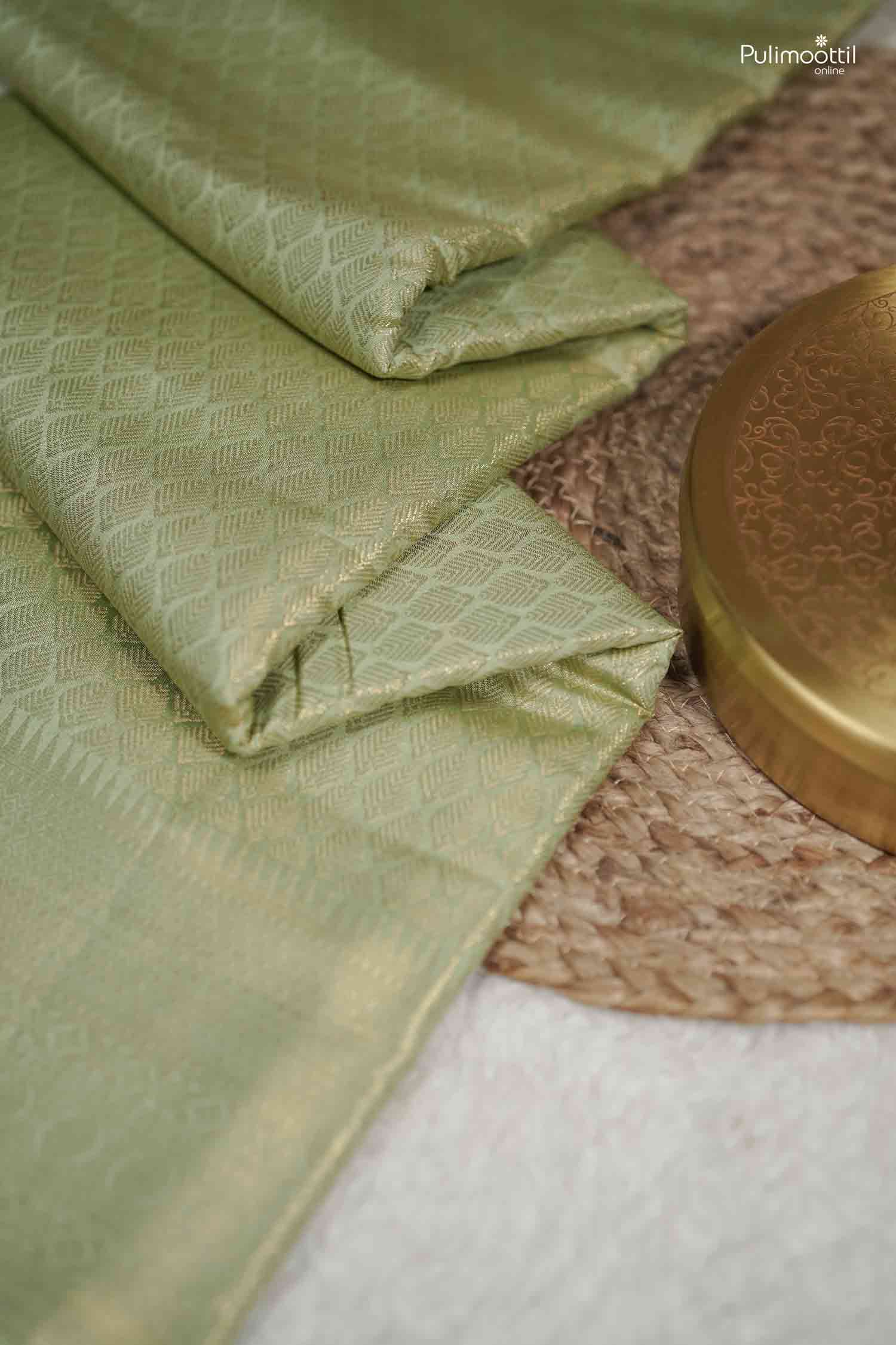 Top-down product image of the neatly folded Pistachio Green Kanchipuram Saree on a textured mat beside a decorative gold box