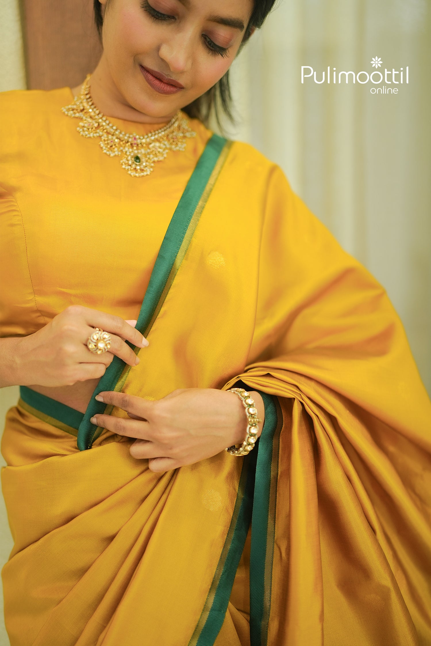 Close-up of the Mustard Yellow Kanchipuram Saree with subtle woven buttas, highlighting the model's pearl and stone necklace, and bracelet.