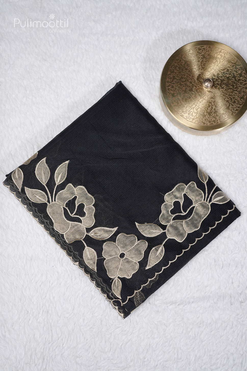 Folded black netcotta saree blouse piece with beige floral applique and scallop border on white background.