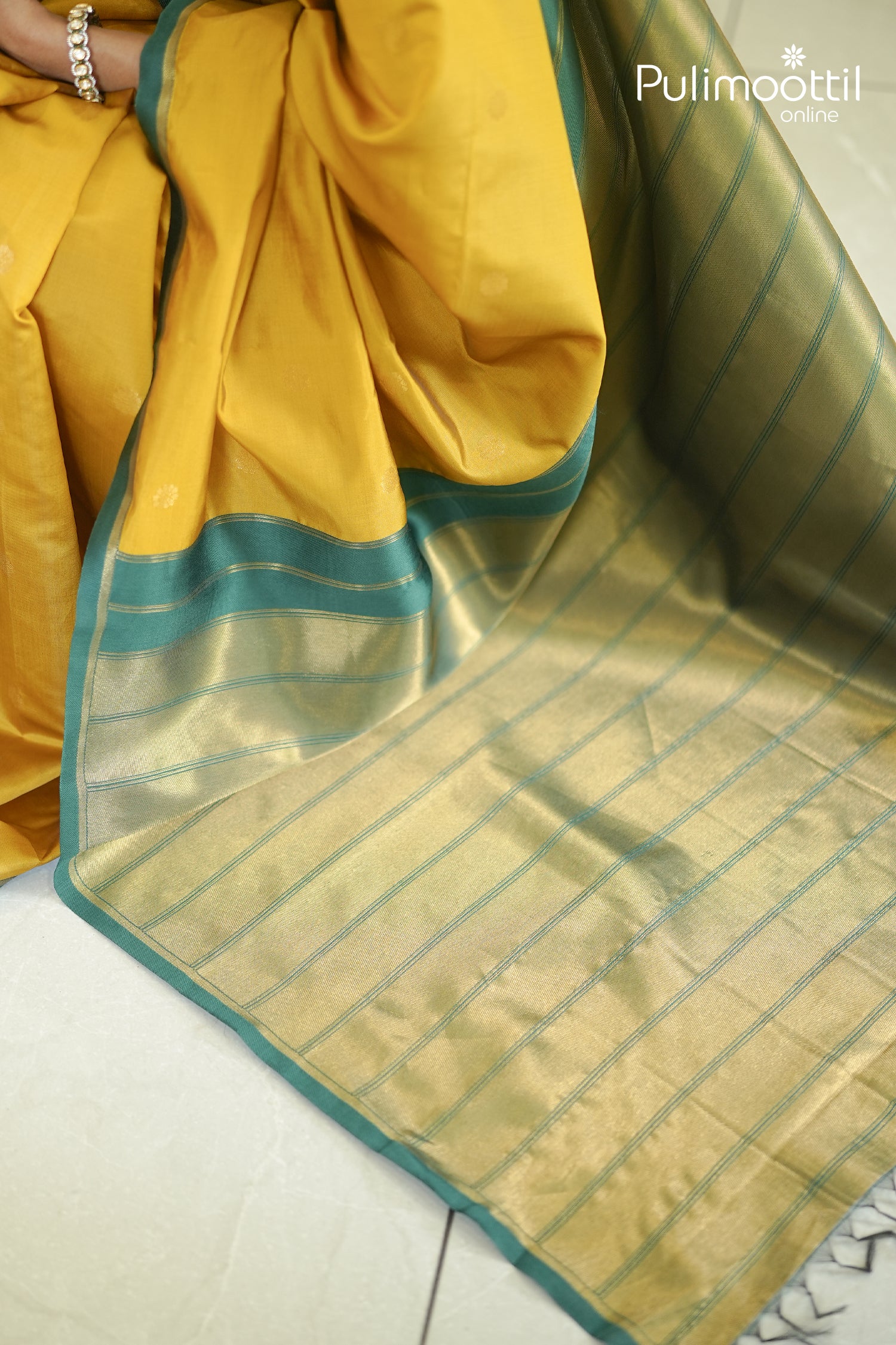 Mid-section close-up of the saree's drape and pleats, clearly showing the Mustard Yellow fabric, Teal Green border, and gold pallu weave