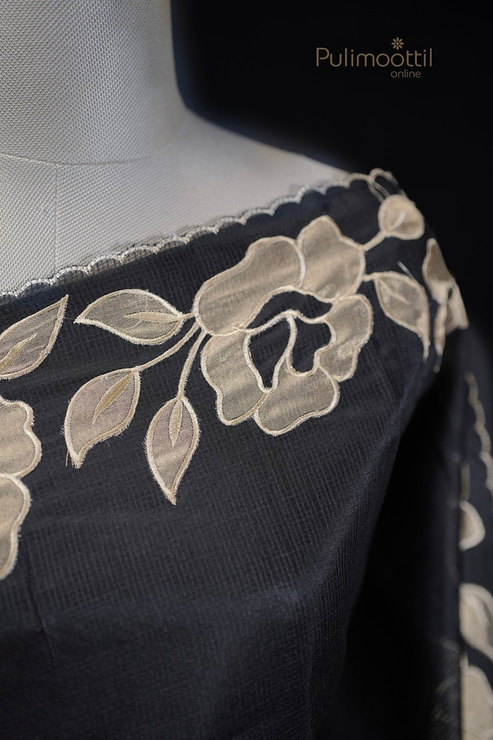 Close-up of black netcotta saree showing detailed beige floral applique and scallop border on fabric.